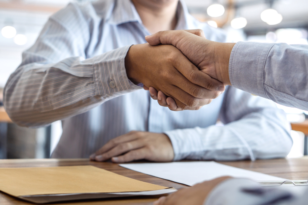 Handshake of two happy business people with documents on the desk